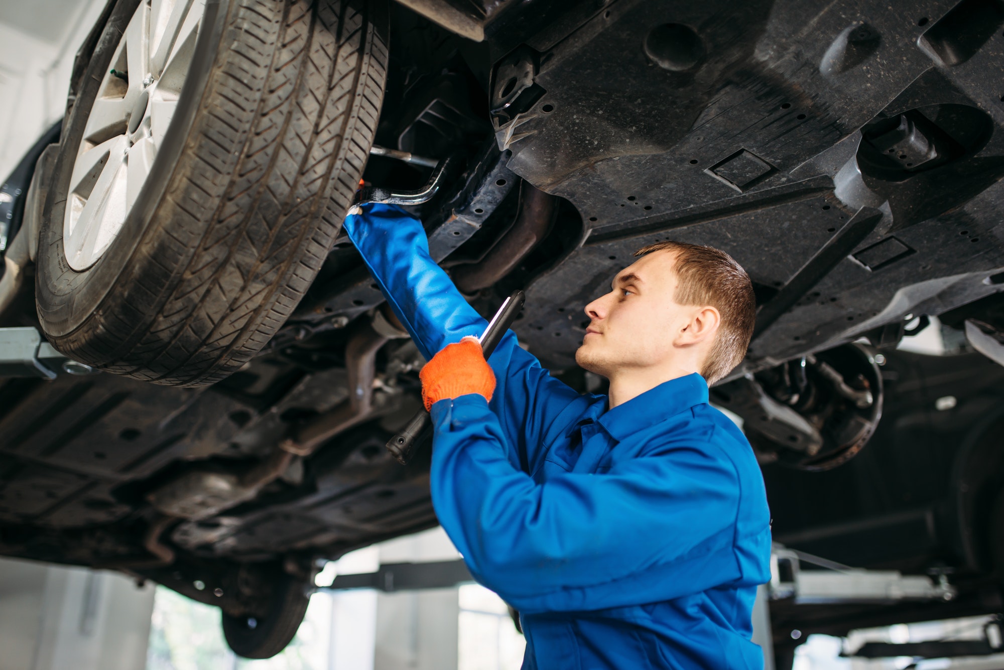 Mechanic with lamp checks car brake hoses